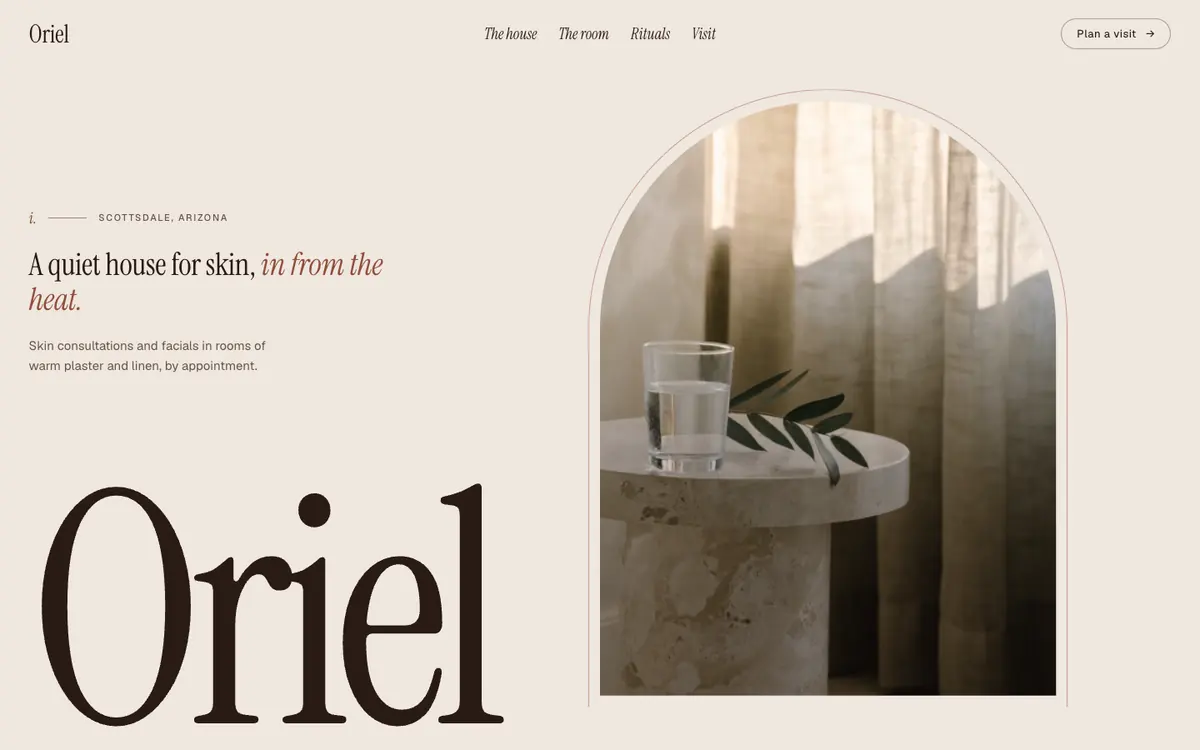 The Oriel sample site: a sunlit lounge with a travertine side table seen through a tall arched window, beside a large serif Oriel wordmark.